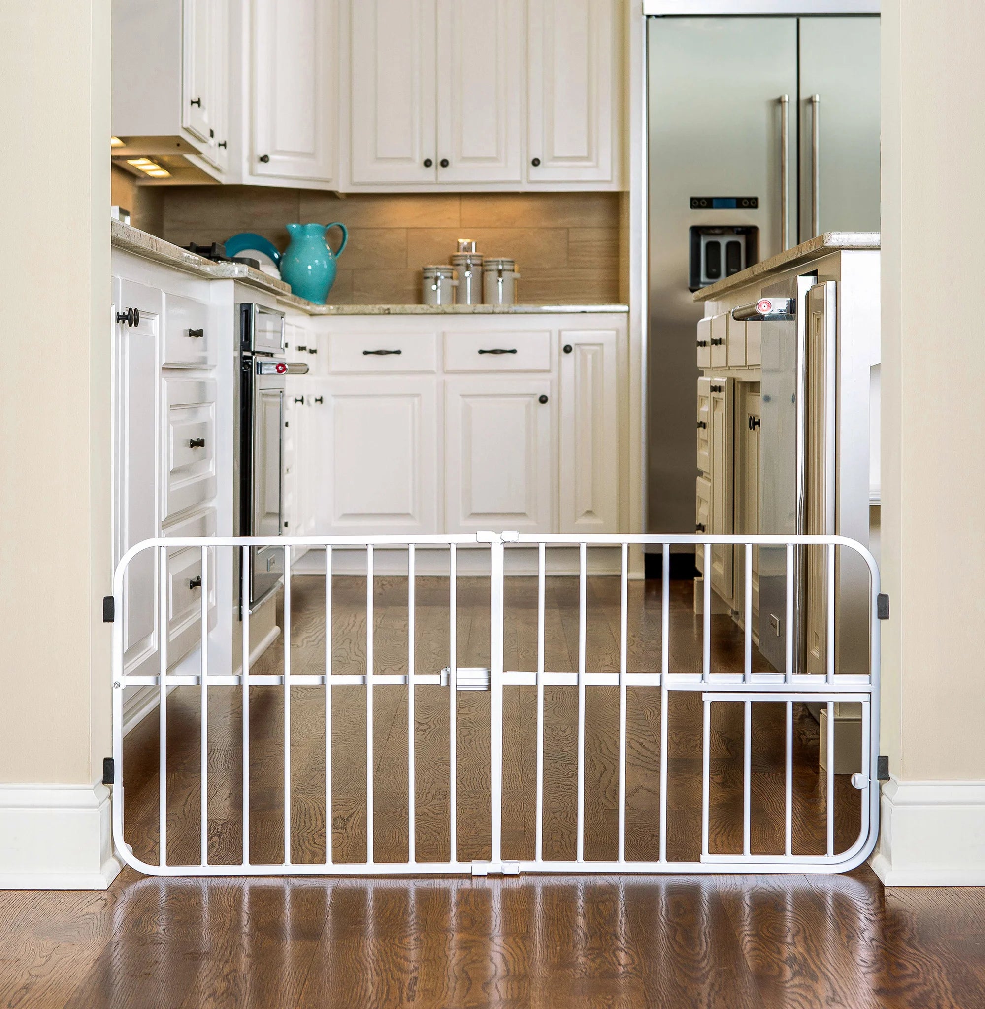 White Carlson Lil Tuffy® Expandable Pet Gate with small pet door, designed for small dogs and pets. The gate stands 18” tall and expands to fit openings between 22” to 38”. It features a sturdy all-metal frame and a pressure-mount system with rubber bumpers to protect walls.