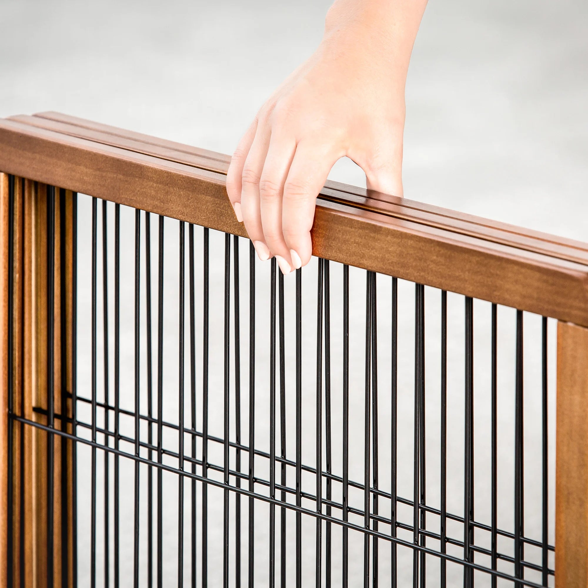 A wooden pet gate with a black metal frame, featuring three panels that fold for easy storage. It stands 20 inches tall, adjusts from 22 to 62 inches wide, and includes a small pet door for dogs to pass through. Ideal for hallways, doorways, or stairs, and requires no permanent installation.
