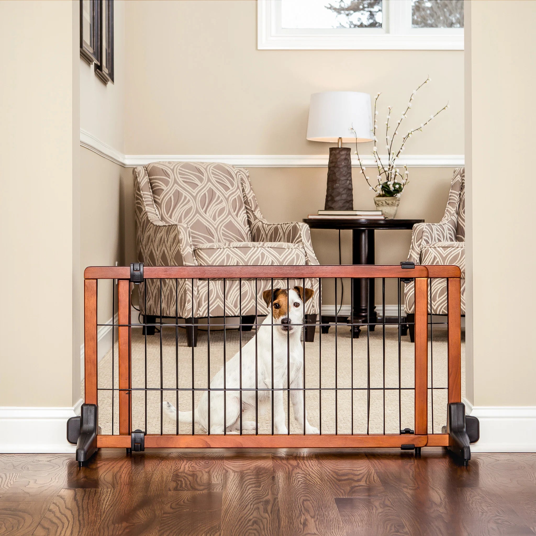 Dog sitting behind Design Paw Extra Wide Freestanding Pet Gate in living room.