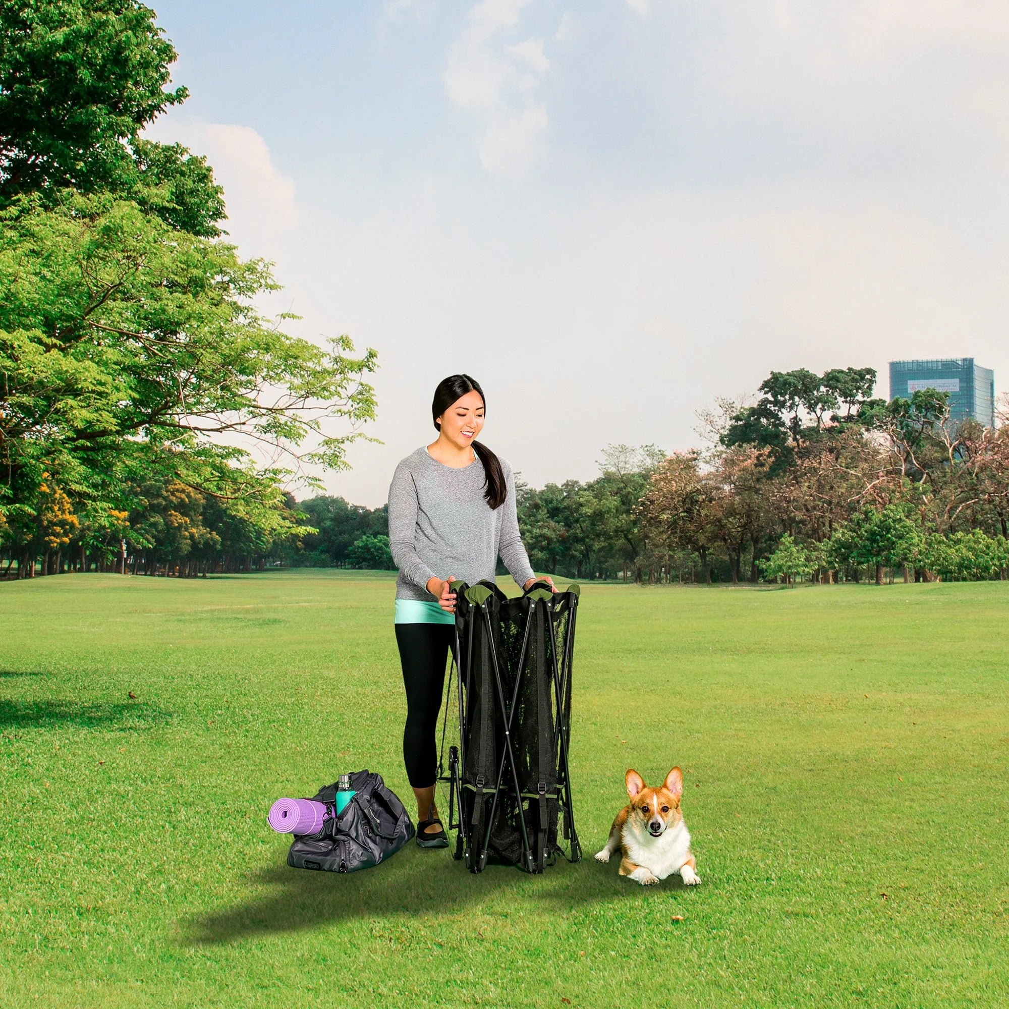 Woman folding Portable Pet Pen on green grass next to her dog in a park.