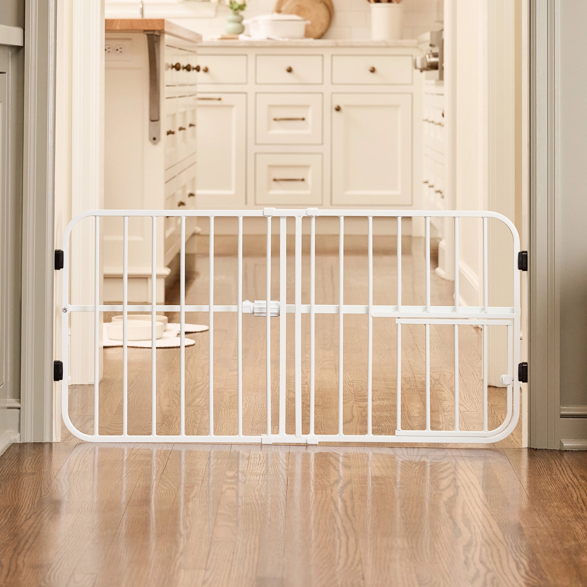 White pet gate in a kitchen setting with wooden flooring and cabinets.