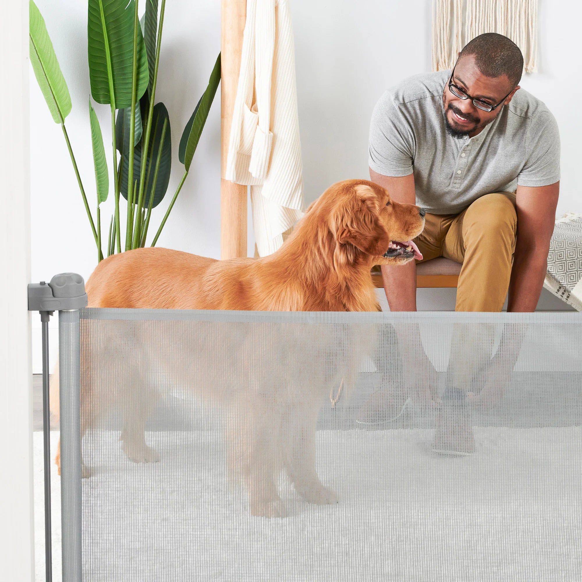 Dog looking at owner who is tying his shoes behind Retractable Pet Gate in mud room.