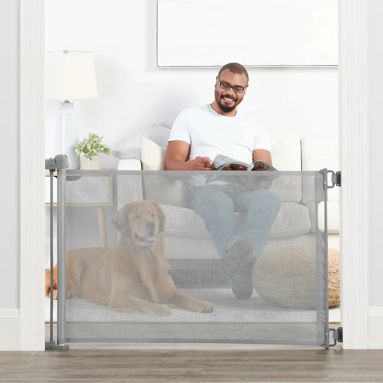 Man sitting on couch next to dog behind Retractable Pet Gate.