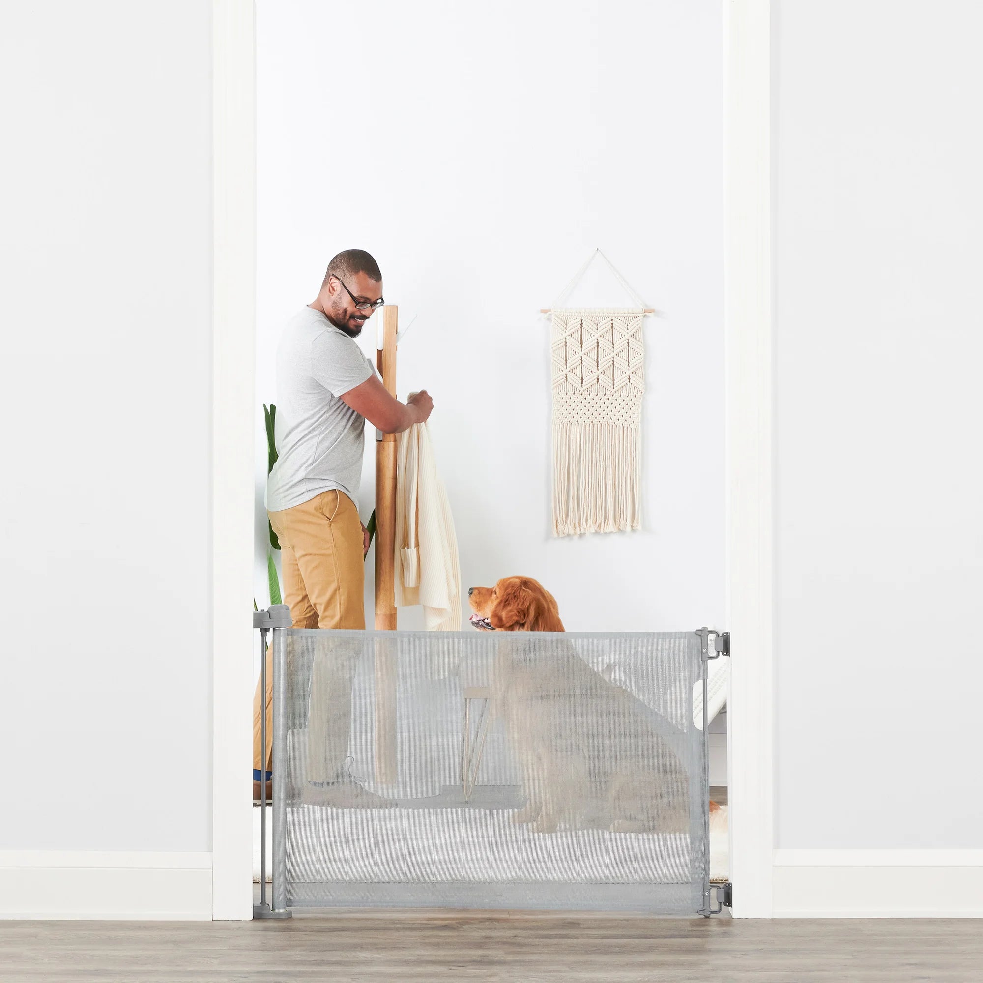 Man looking at dog while grabbing coat in mudroom behind Retractable Pet Gate.