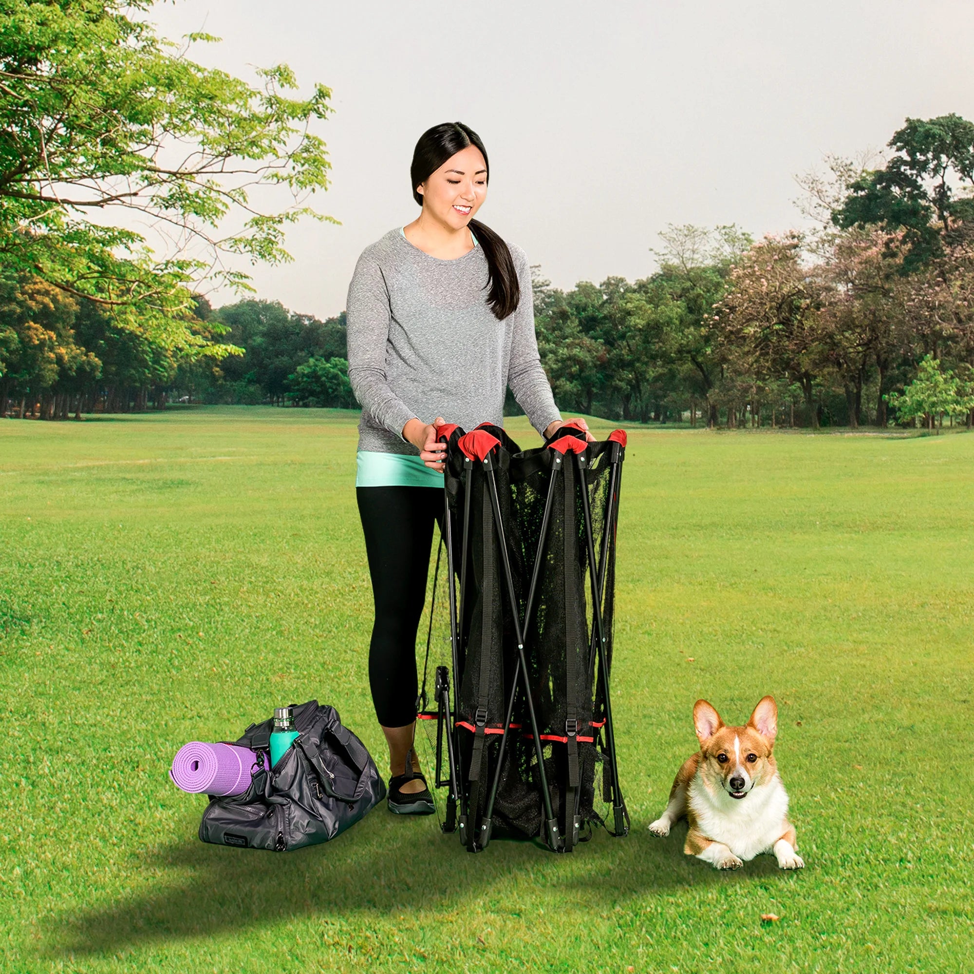 Woman looking down at dog while holding Portable Pet Pen at park.