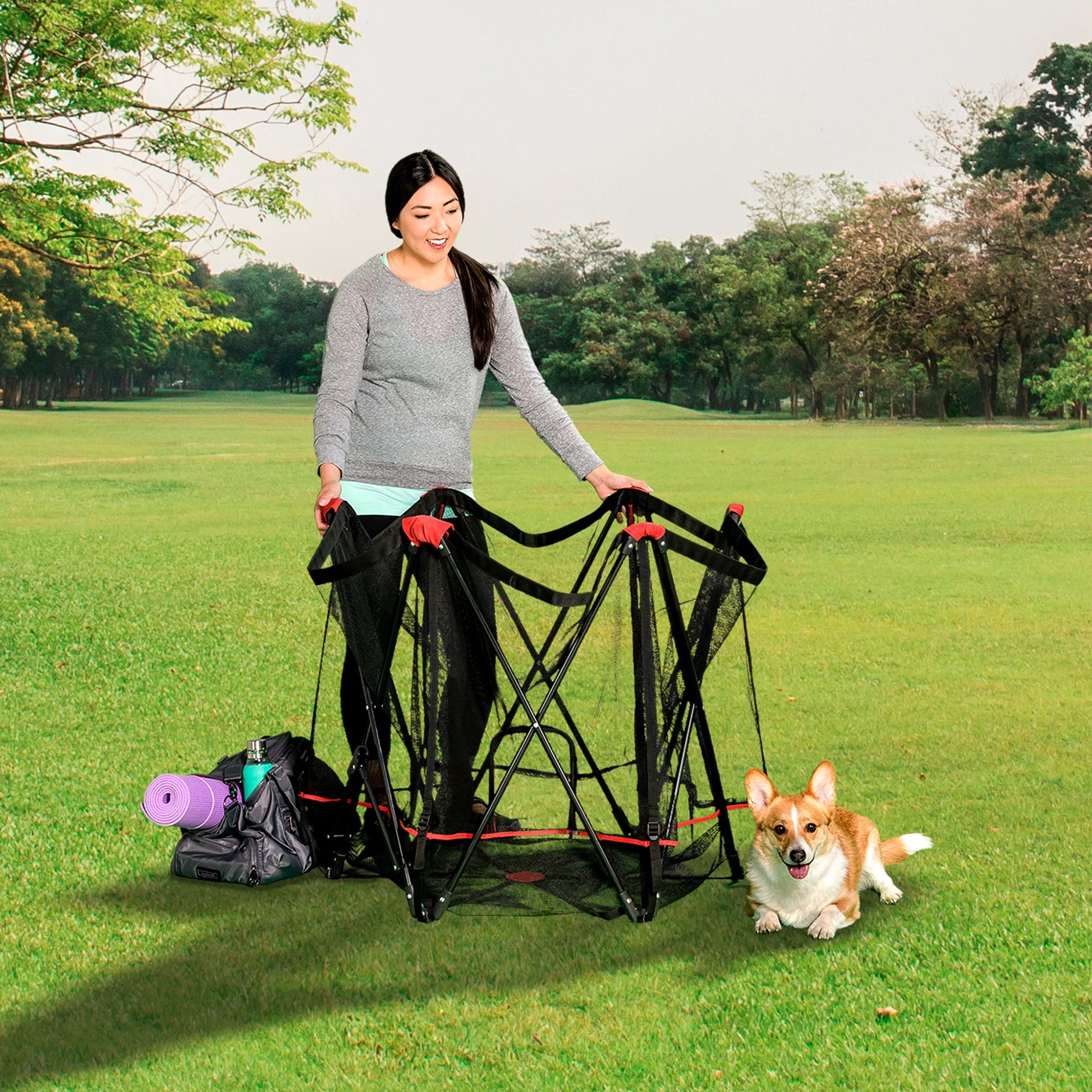 Woman at park setting up Portable Pet Pen while dog sits on the ground.