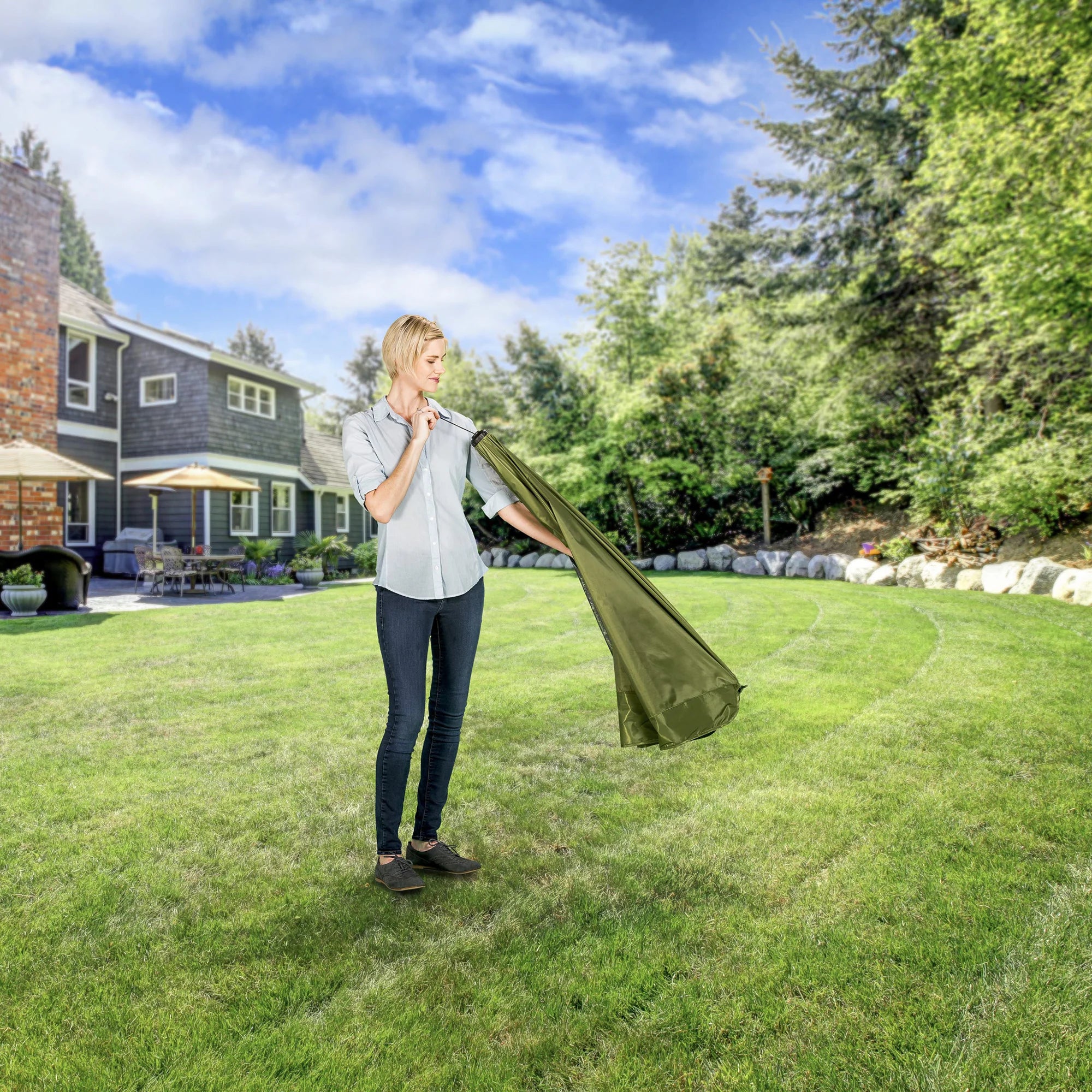 A woman folding the Canopy of the Portable Pet Pen on a green space in a backyard.