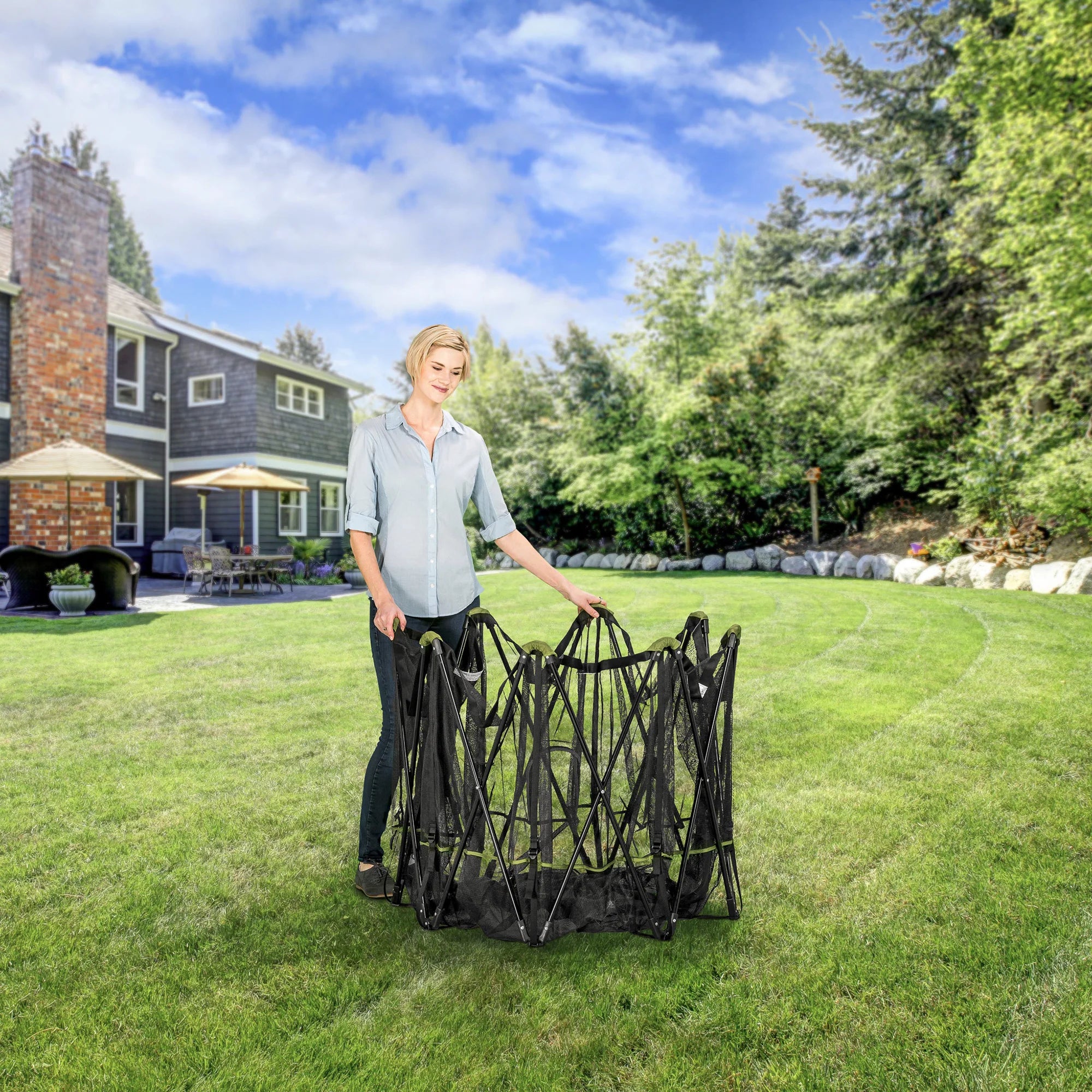 A woman folding up the Portable Pet Pen on green grass in a backyard.