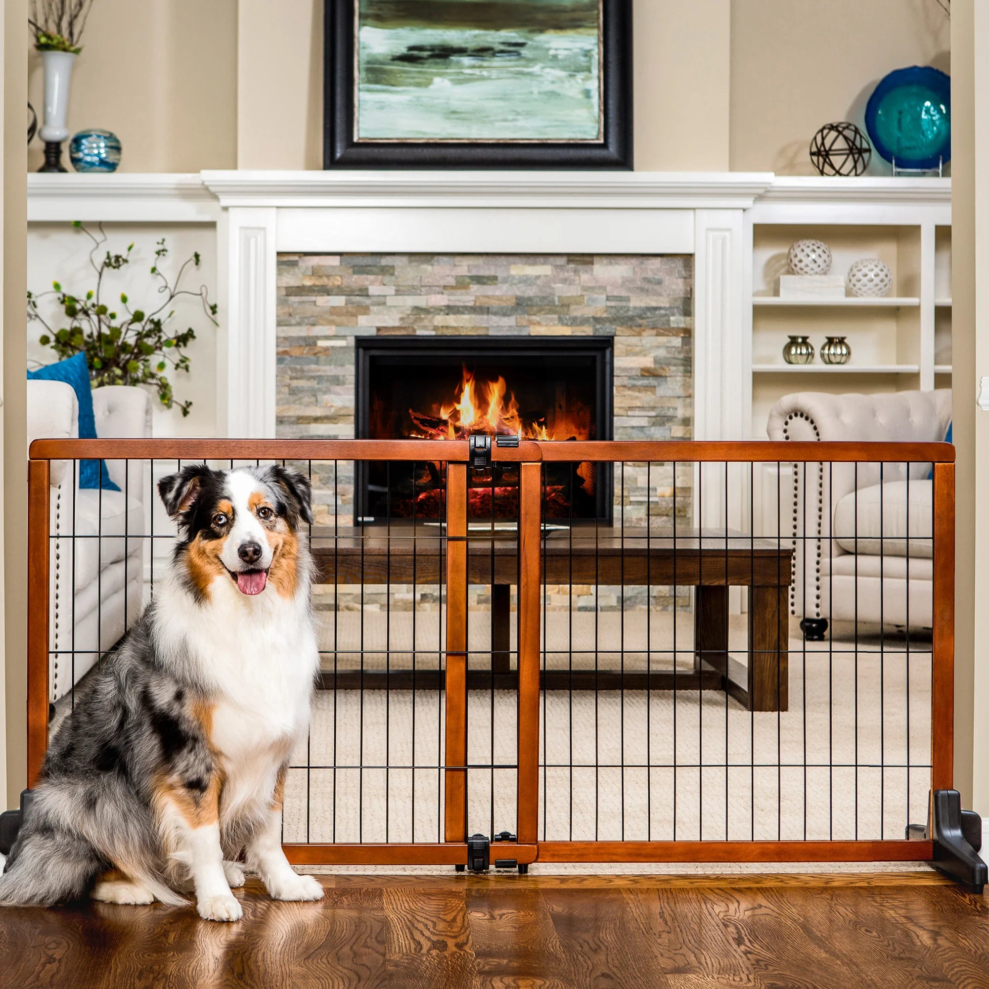 A dog sitting in front of the Design Paw Extra Tall Extra Wide Freestanding Pet Gate in a living room.