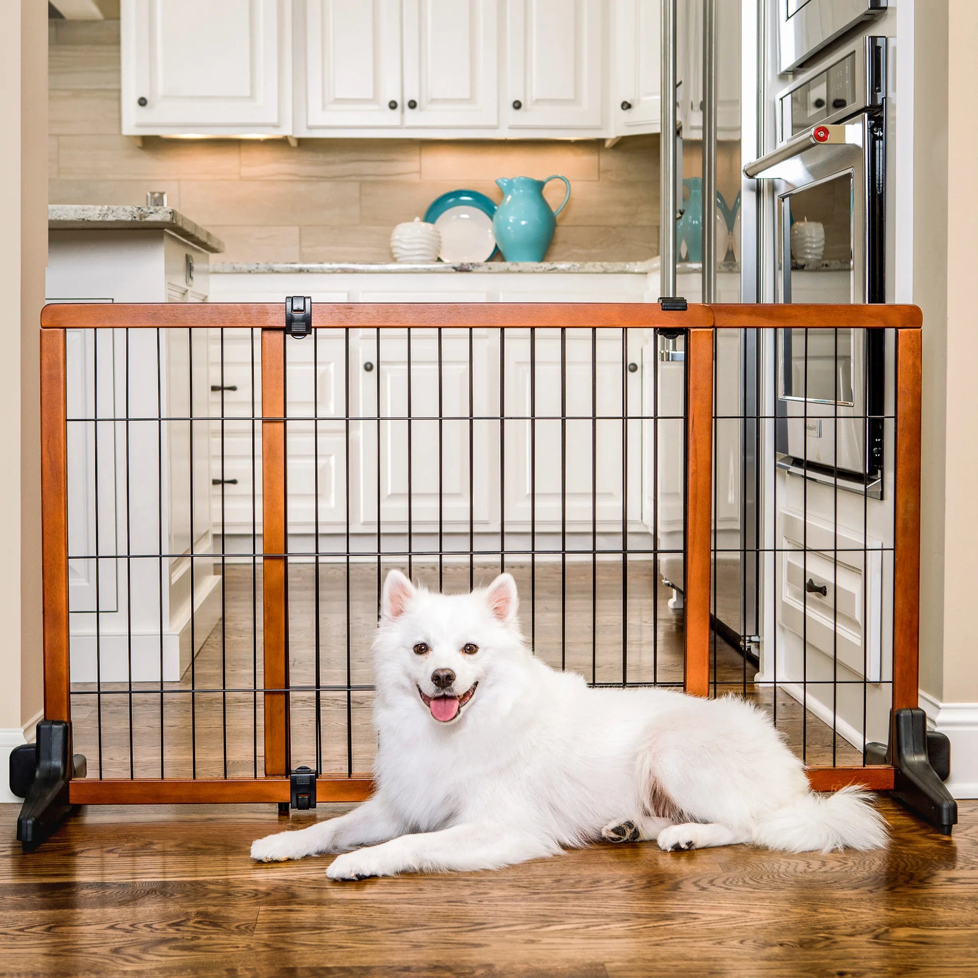 Dog sitting in front of the Design Paw Extra Tall Extra Wide Freestanding Pet Gate in a kitchen.