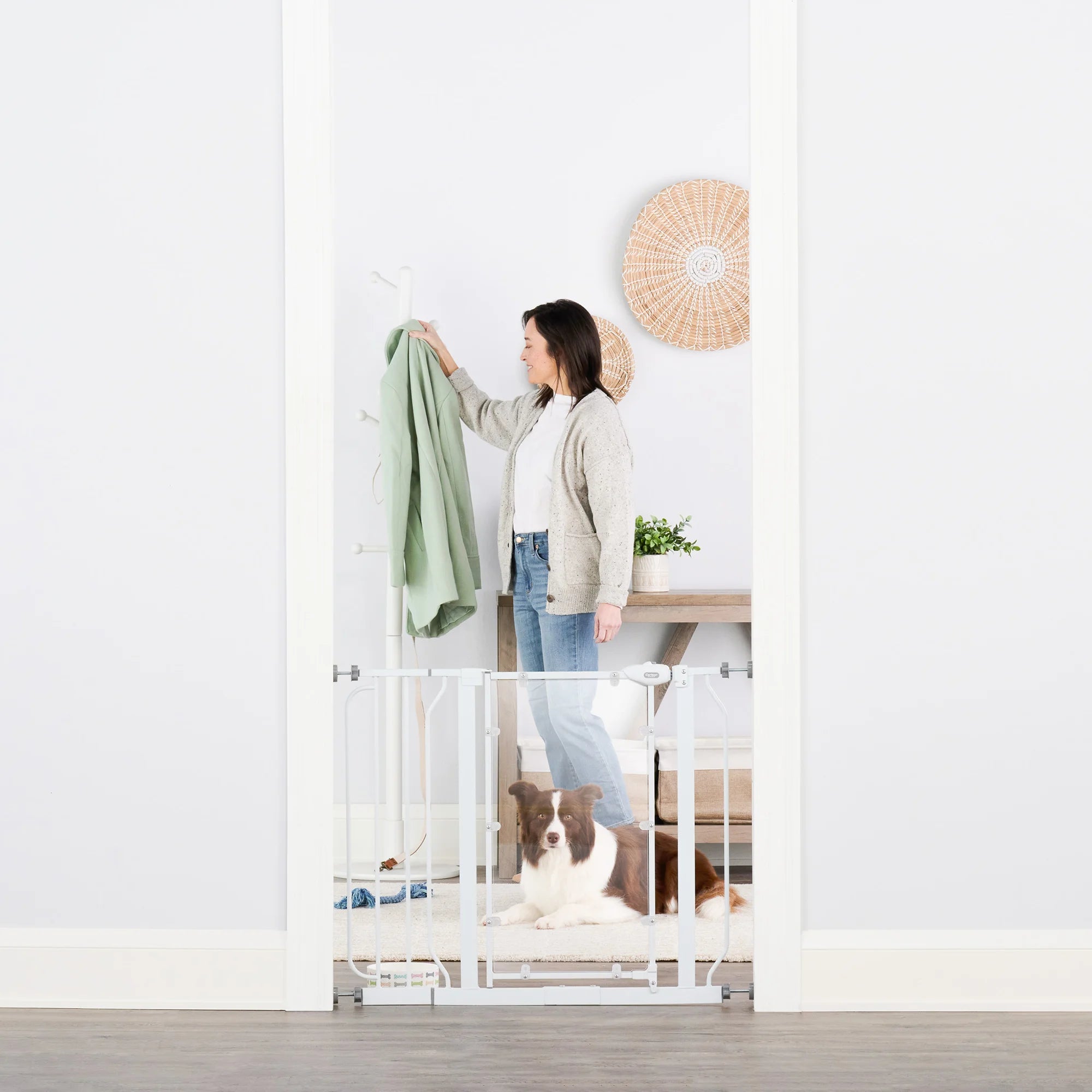 Woman hanging up coat next to dog behind Direct View™ Pet Gate.