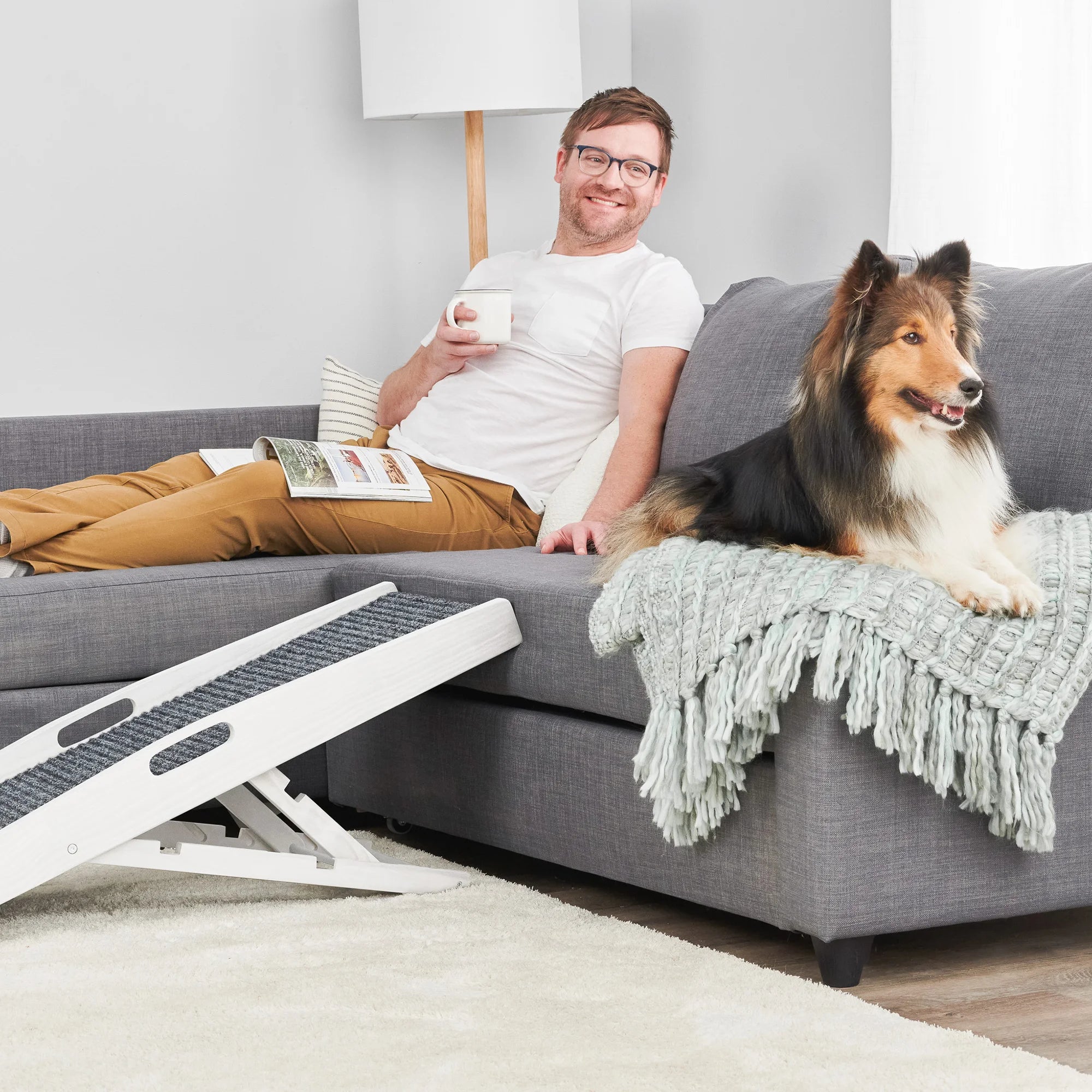 Man sitting on his couch with his dog next to a Carlson Indoor Pet Ramp.