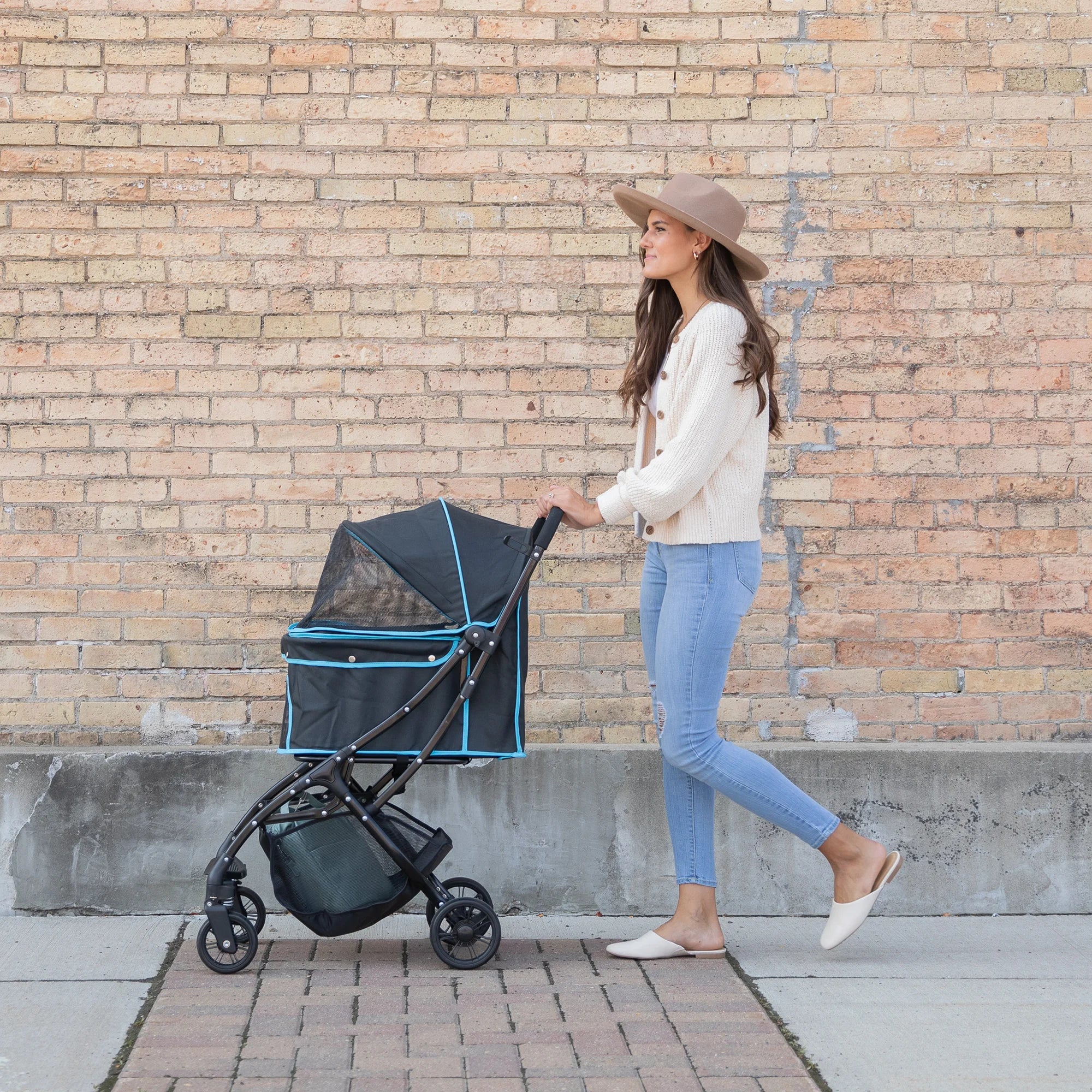 Woman with brown hair walking her black and white cat outside in an Easy Fold & Go Pet Stroller in front of a brick wall.