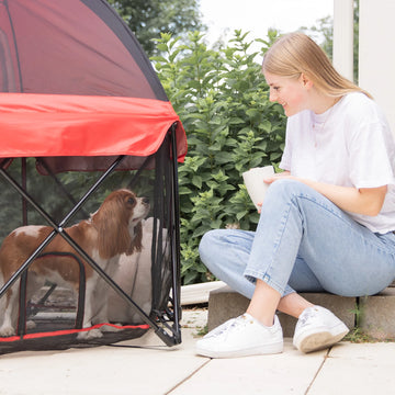 Woman holding coffee cup while looking at her dog that is in the Portable Pet Pen with Canopy while outside.