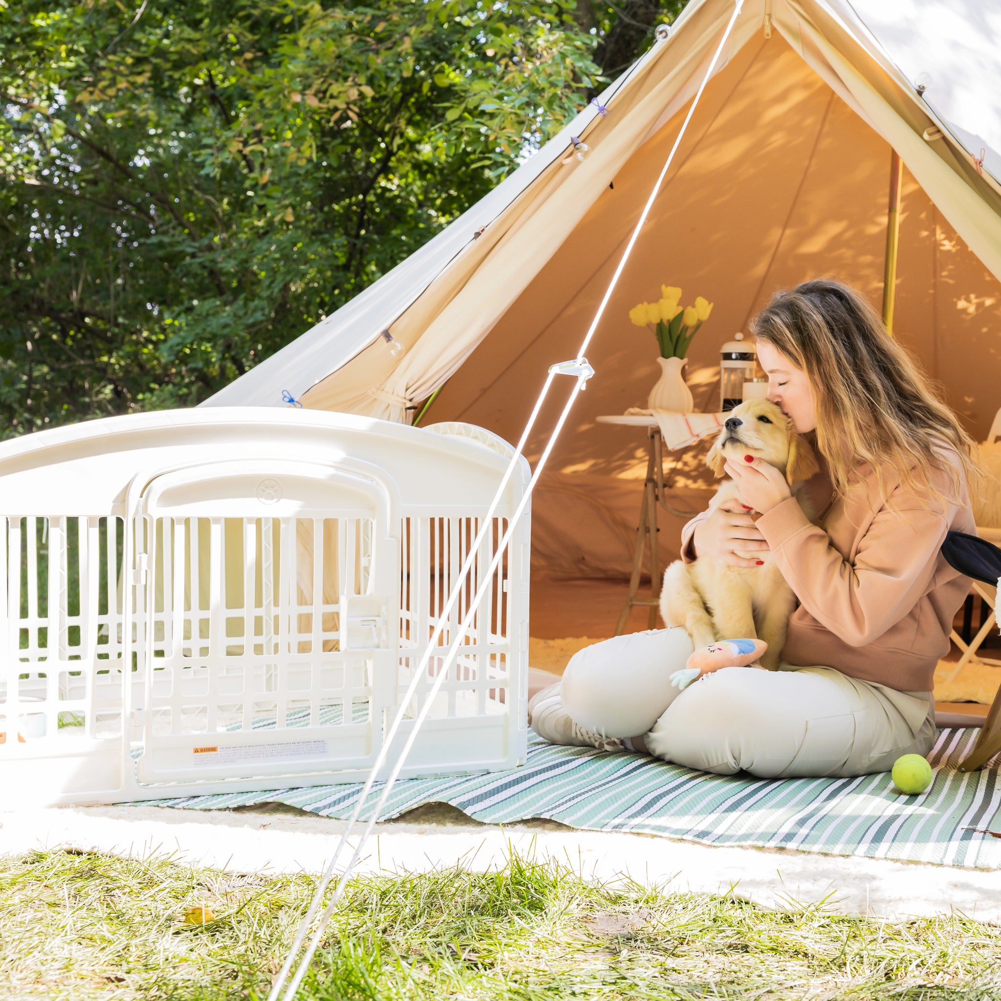 Woman sitting outside a tent with a dog, surrounded by nature.
